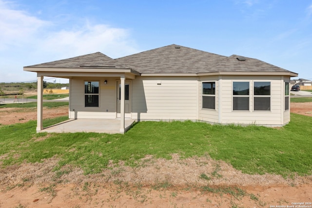 back of house with a patio area, a lawn, and a shingled roof