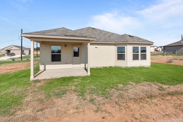 back of property with a patio area, a lawn, and roof with shingles