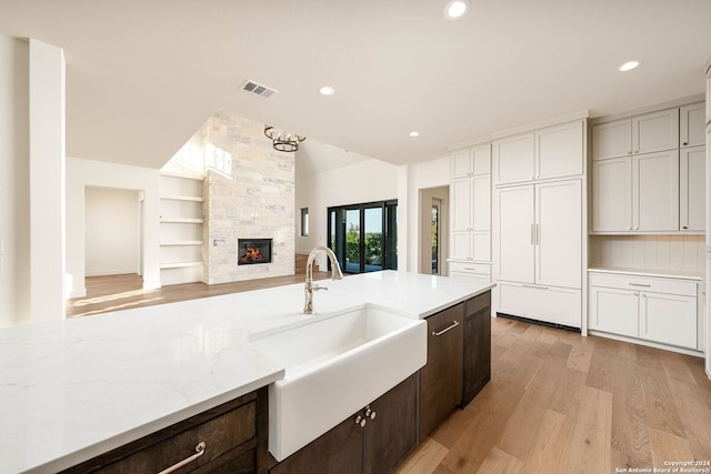 kitchen featuring light hardwood / wood-style flooring, dark brown cabinets, sink, white cabinets, and a fireplace