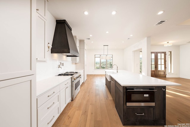 kitchen with wall chimney range hood, appliances with stainless steel finishes, plenty of natural light, and a center island with sink