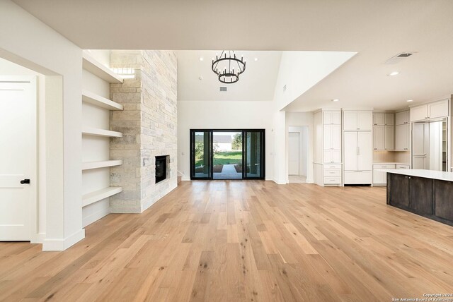 unfurnished living room with vaulted ceiling, a stone fireplace, light hardwood / wood-style flooring, and built in shelves