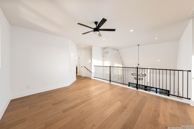 empty room featuring light hardwood / wood-style flooring, lofted ceiling, and ceiling fan with notable chandelier