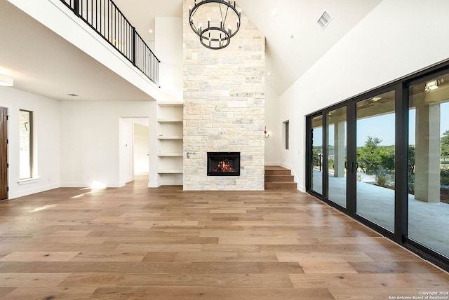 unfurnished living room with a fireplace, light hardwood / wood-style flooring, a notable chandelier, built in shelves, and a towering ceiling