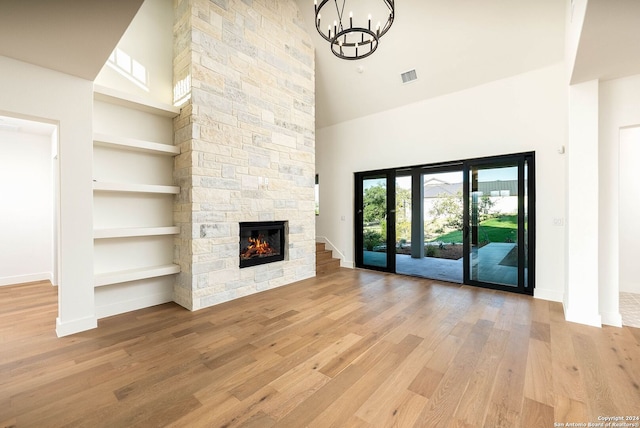 unfurnished living room featuring light hardwood / wood-style floors, a towering ceiling, a fireplace, and built in shelves