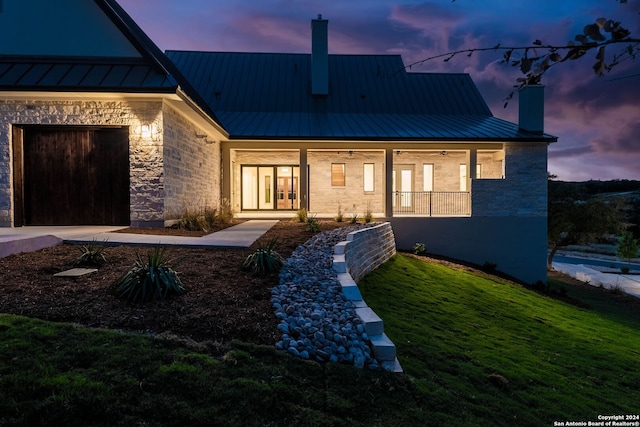 back house at dusk featuring covered porch and a lawn