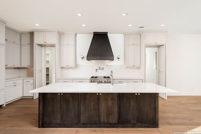 kitchen featuring hardwood / wood-style flooring, an island with sink, custom range hood, sink, and white cabinets