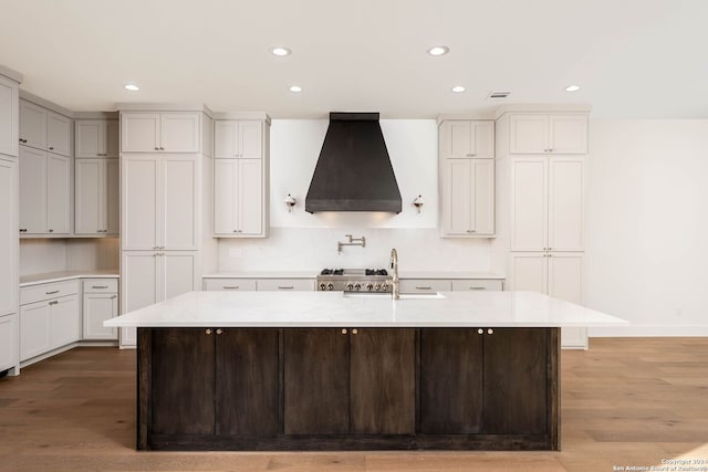 kitchen featuring wood-type flooring, sink, stainless steel range oven, premium range hood, and a center island with sink