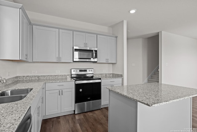 kitchen featuring sink, a center island, dark wood-type flooring, light stone counters, and appliances with stainless steel finishes