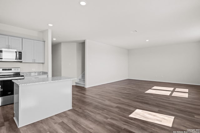 kitchen with appliances with stainless steel finishes, dark hardwood / wood-style floors, a kitchen island, and light stone counters