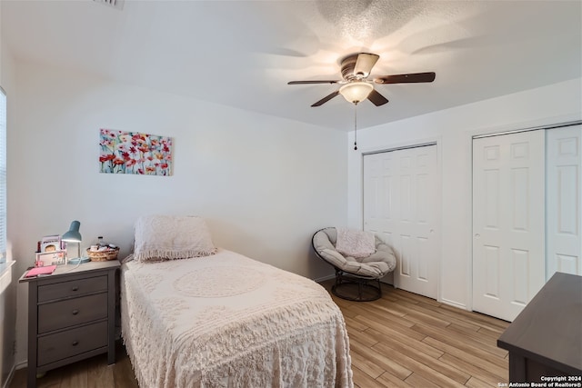 bedroom with ceiling fan, light hardwood / wood-style floors, and two closets