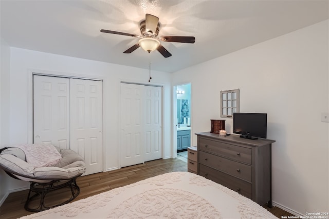 bedroom with multiple closets, ensuite bathroom, ceiling fan, and dark hardwood / wood-style floors