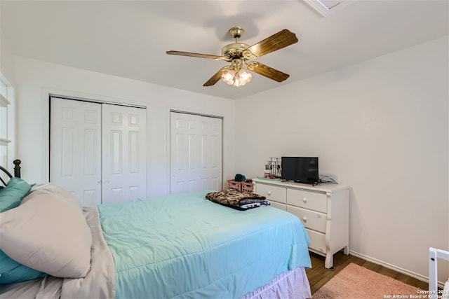 bedroom with dark hardwood / wood-style floors, ceiling fan, and two closets