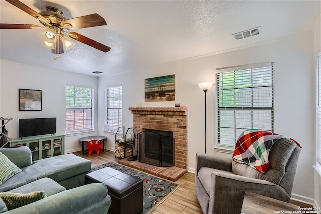 living room featuring ceiling fan, a fireplace, a textured ceiling, and light wood-type flooring