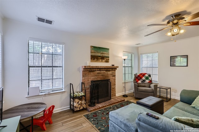 living room featuring a fireplace, a textured ceiling, light hardwood / wood-style flooring, and ceiling fan