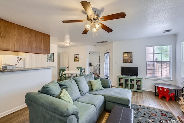 living room with a textured ceiling, ceiling fan, and dark wood-type flooring