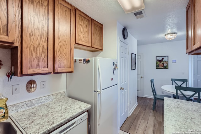 kitchen featuring a textured ceiling, light stone countertops, light hardwood / wood-style floors, and white appliances