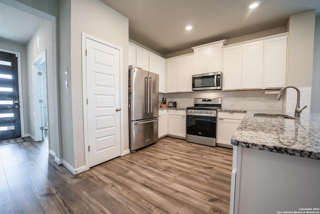 kitchen featuring light stone countertops, sink, appliances with stainless steel finishes, white cabinets, and light wood-type flooring