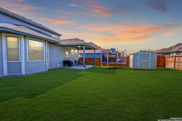 yard at dusk featuring a patio area, a trampoline, and a shed