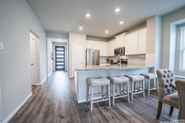 kitchen featuring stainless steel appliances, light stone counters, dark hardwood / wood-style floors, kitchen peninsula, and white cabinets