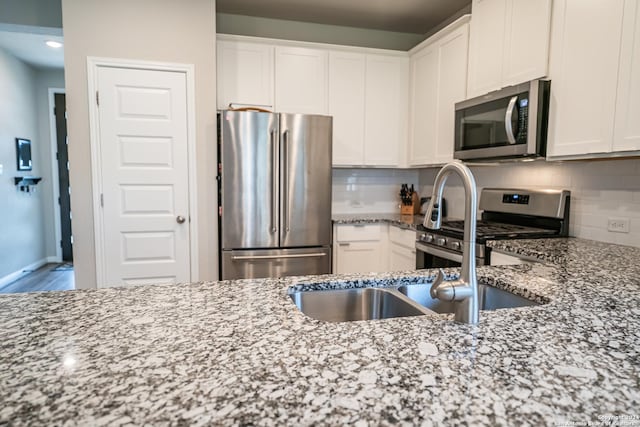 kitchen with decorative backsplash, light stone countertops, white cabinets, and stainless steel appliances