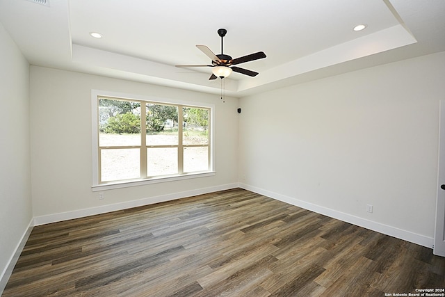 spare room featuring dark wood-type flooring, ceiling fan, and a raised ceiling