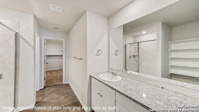 bathroom featuring wood finished floors, visible vents, vanity, a spacious closet, and a shower stall