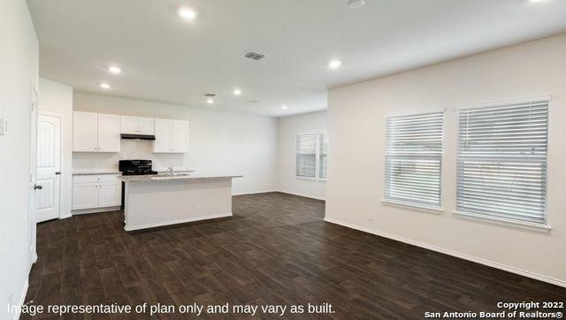 kitchen with stove, dark wood-type flooring, a kitchen island with sink, white cabinetry, and under cabinet range hood