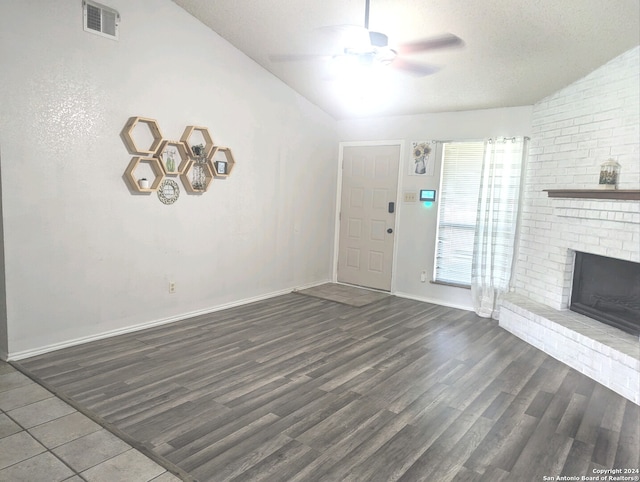 unfurnished living room featuring dark wood-type flooring, a brick fireplace, vaulted ceiling, ceiling fan, and a textured ceiling