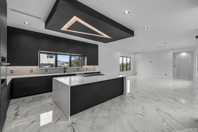 kitchen with a healthy amount of sunlight, backsplash, a spacious island, and sink