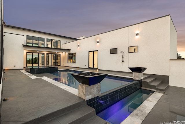 pool at dusk with a patio area and an in ground hot tub