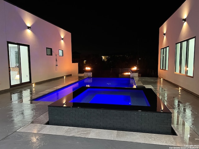 pool at night featuring a patio area and an in ground hot tub