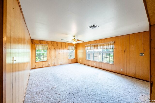 unfurnished room with wood walls, light carpet, plenty of natural light, and ceiling fan