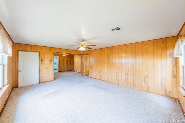 carpeted spare room with wood walls and ceiling fan