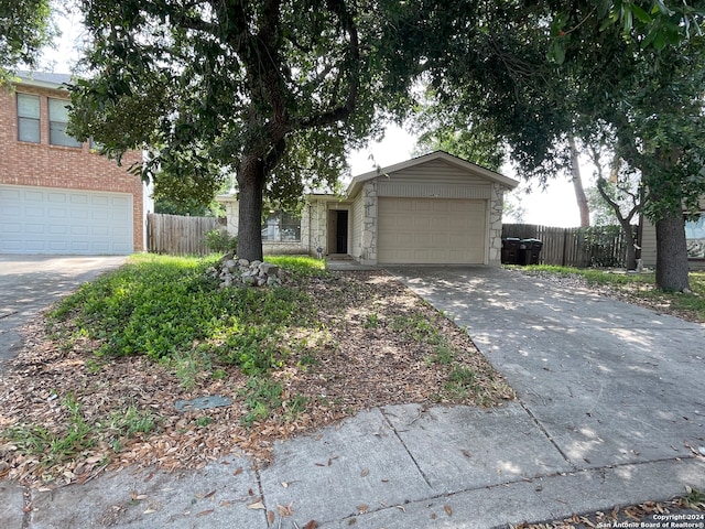 ranch-style home featuring a garage, concrete driveway, stone siding, and fence