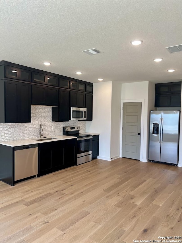 kitchen with backsplash, sink, light wood-type flooring, a textured ceiling, and stainless steel appliances