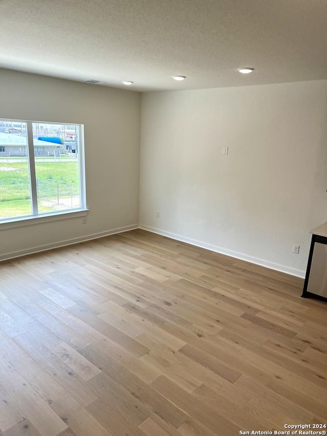 unfurnished room with a textured ceiling and light hardwood / wood-style floors