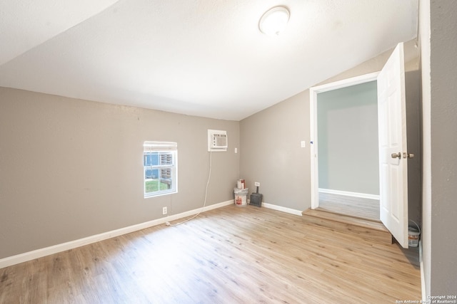 unfurnished room featuring light wood-style floors, baseboards, vaulted ceiling, and a wall mounted AC