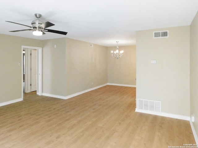 empty room with ceiling fan with notable chandelier and light hardwood / wood-style flooring