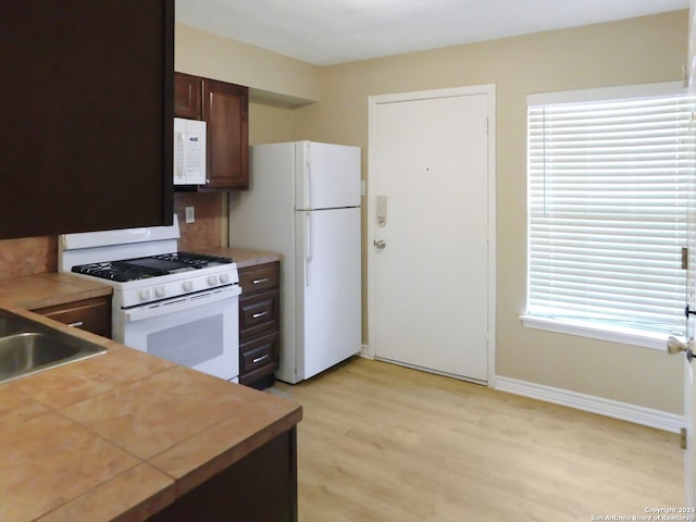 kitchen featuring dark brown cabinets, a healthy amount of sunlight, white appliances, and light hardwood / wood-style flooring