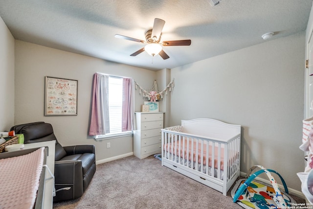 carpeted bedroom featuring a textured ceiling, a nursery area, and ceiling fan