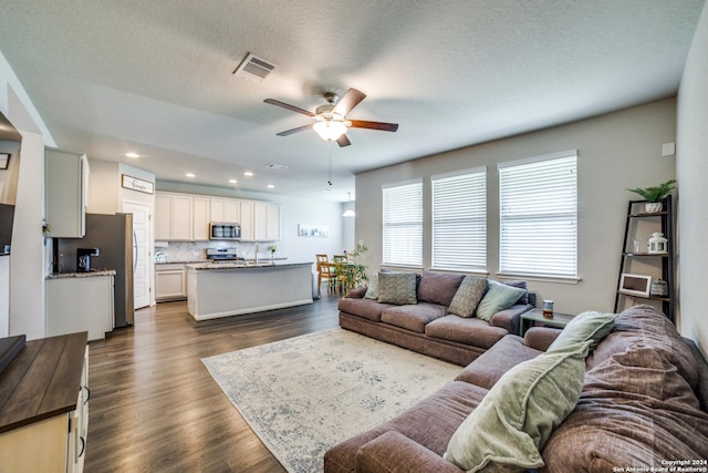 living room with a textured ceiling, ceiling fan, sink, and dark wood-type flooring