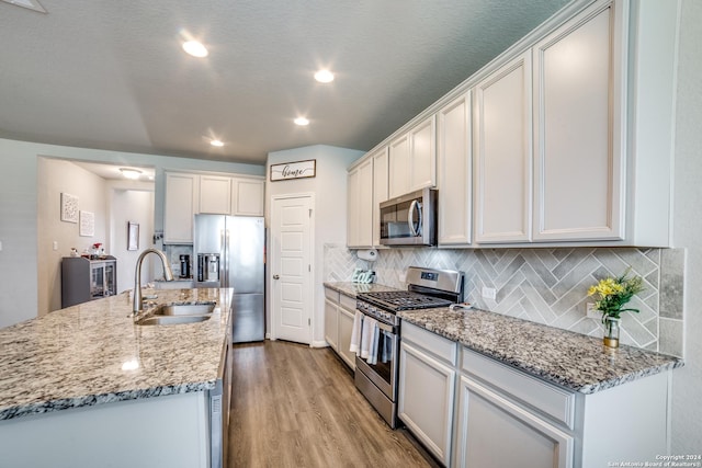 kitchen with white cabinetry, sink, stainless steel appliances, an island with sink, and light wood-type flooring