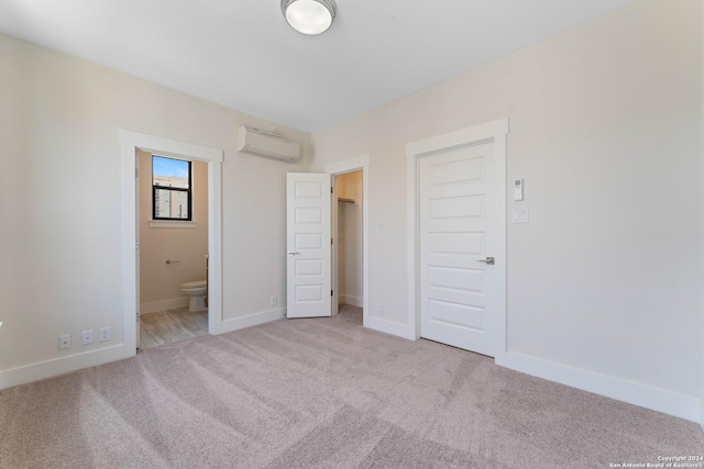 unfurnished bedroom featuring light carpet, ensuite bathroom, a wall unit AC, and a closet