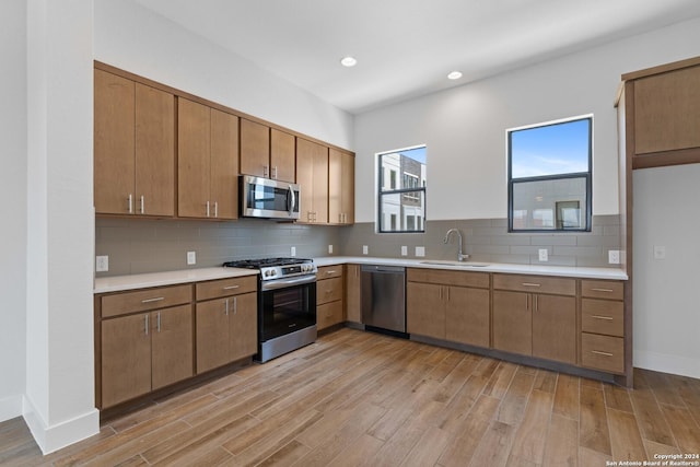 kitchen with backsplash, sink, stainless steel appliances, and light wood-type flooring