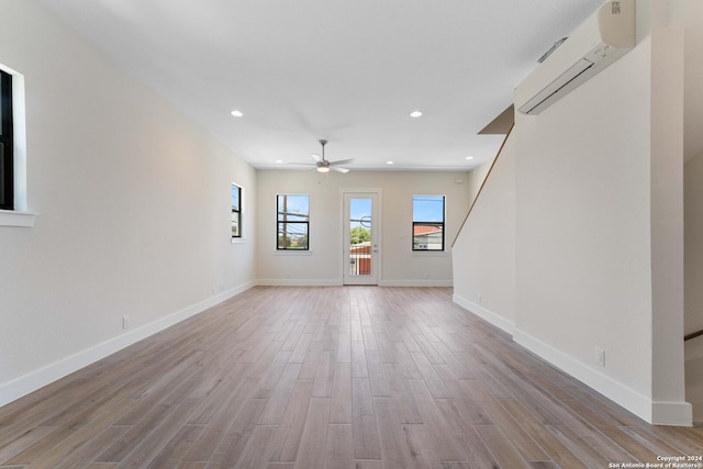 unfurnished living room featuring an AC wall unit, ceiling fan, and light hardwood / wood-style floors