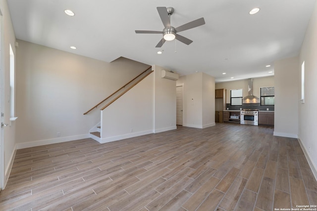 unfurnished living room with a wall mounted air conditioner, light hardwood / wood-style floors, and ceiling fan