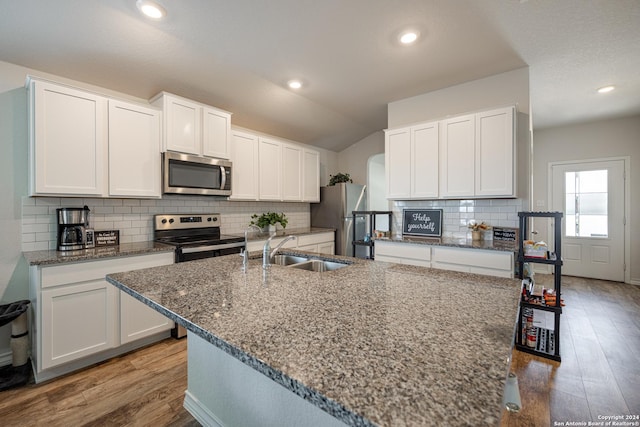 kitchen with white cabinetry, sink, stainless steel appliances, an island with sink, and vaulted ceiling