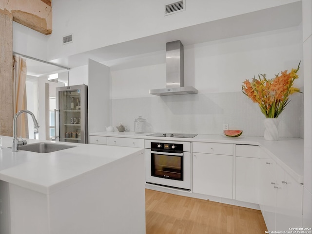 kitchen with white cabinets, wall chimney range hood, sink, black electric cooktop, and wall oven