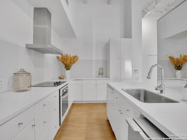 kitchen with white cabinetry, sink, stainless steel oven, wall chimney range hood, and black electric cooktop