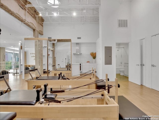 exercise room with electric panel, hardwood / wood-style floors, and a towering ceiling